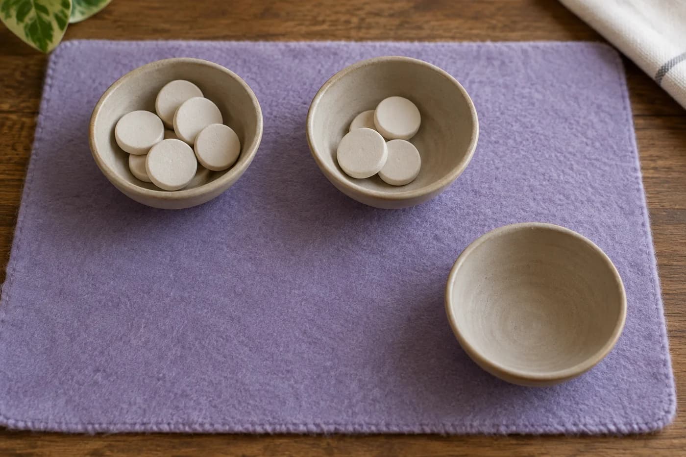 Unglazed bowls and ivory clay discs form separate groups on lavender felt beside one empty shallow bowl