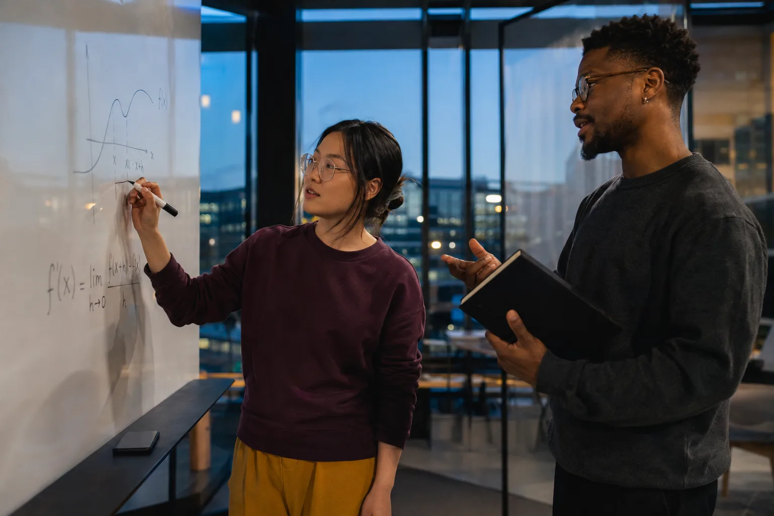 Two adult learners discussing a product rule derivative on a glass writing board